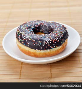sweet donut with chocolate icing and colored sugar on wooden background