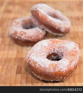 Sweet donuts sprinkled with sugar on wooden tray.