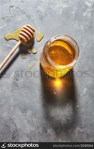 Sweet floral natural honey full a jar and wooden spoon on a gray concrete table, copy space., pure natural sweet goodness. Jewish rosh hashanah holiday concept.. Wooden stick on a spilled honey on the table and glass pot with natural meadow sweet dessert on a gray kitchen table. Pure natural sweet goodness.
