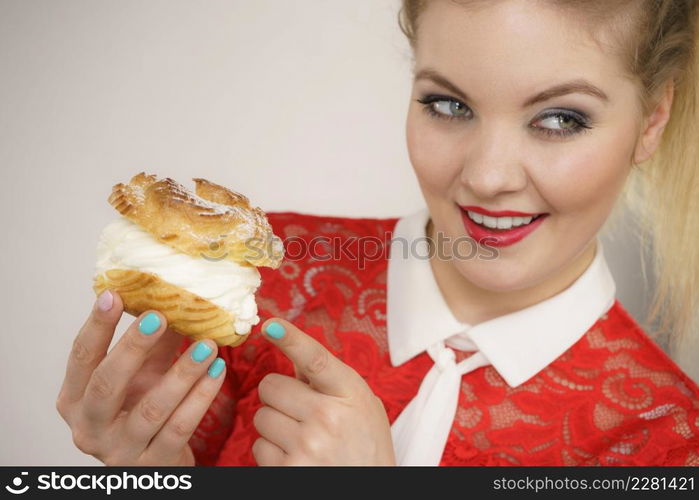 Sweet food and happiness concept. Funny joyful blonde woman holding yummy choux puff cake with whipped cream, excited face expression. On grey. Smiling woman holds cream puff cake