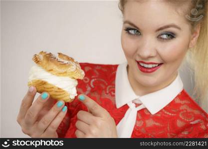 Sweet food and happiness concept. Funny joyful blonde woman holding yummy choux puff cake with whipped cream, excited face expression. On grey. Smiling woman holds cream puff cake