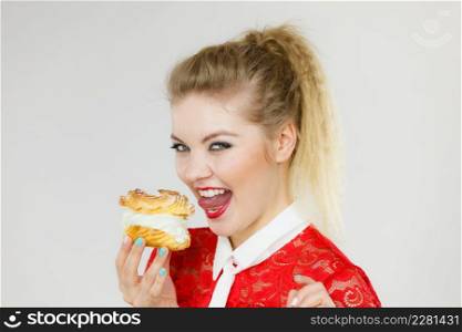 Sweet food and happiness concept. Funny joyful blonde woman holding yummy choux puff cake with whipped cream, excited face expression. On gray. Funny woman holds cream puff cake