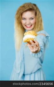 Sweet food and happiness concept. Funny joyful blonde woman holding yummy choux puff cake with whipped cream, excited face expression. On blue. Funny woman holds cream puff cake