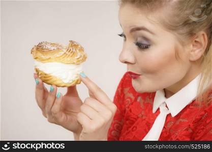 Sweet food and happiness concept. Funny joyful blonde woman holding yummy choux puff cake with whipped cream, excited face expression. On grey. Funny woman holds cream puff cake