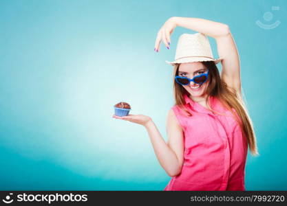 sweet food happiness and people concept. Smiling summer fashionable woman wearing straw hat heart shaped sunglasses holds cake cupcake in hand blue background