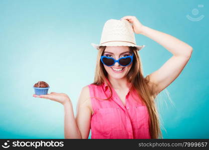 sweet food happiness and people concept. Smiling summer fashionable woman wearing straw hat heart shaped sunglasses holds cake cupcake in hand blue background