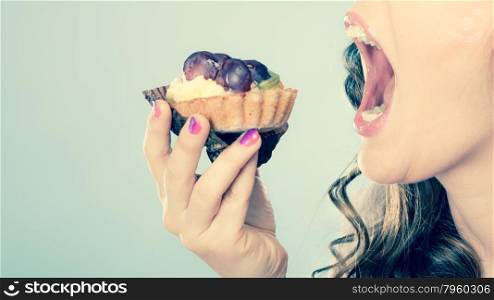 Sweet food indulging and fattening concept. Woman face profile wide open mouth eating cake cupcake filtered photo