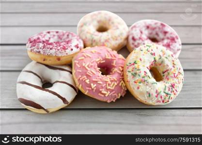 sweet food, junk-food and unhealthy eating concept - close up of glazed donuts over grey wooden boards background. close up of glazed donuts on wooden boards
