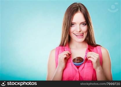 sweet food or sex for brighten moods. Smiling woman having fun holds chocolate muffin cake on her chest blue background