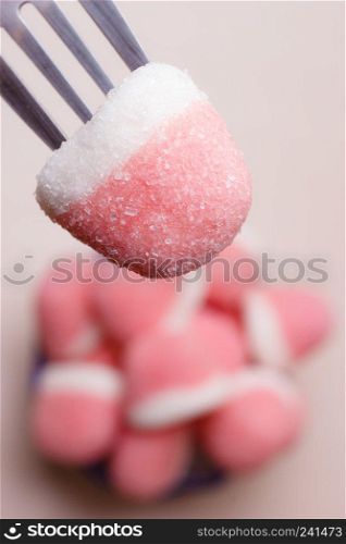 Sweet food. Pink gummy sweets with sugar closeup. Hand holds fork reaching out to take candy from bowl, top view
