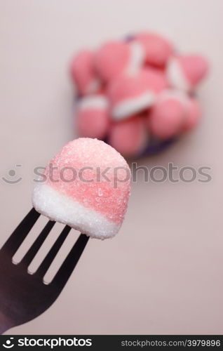 Sweet food. Pink gummy sweets with sugar closeup. Hand holds fork reaching out to take candy from bowl, top view