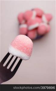 Sweet food. Pink gummy sweets with sugar closeup. Hand holds fork reaching out to take candy from bowl, top view
