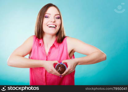 Sweet food sugar make us happy. Smiling woman holds chocolate muffin in hand making heart shape with fingers around cake blue background