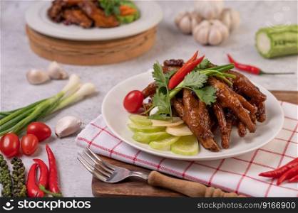 Sweet fried chicken feet in a white plate with coriander, chili, cucumber, and tomato.