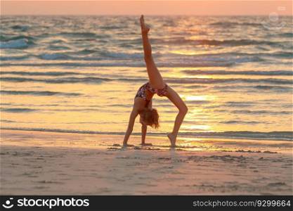 Sweet girl doing yoga on the beach over sunset sky background. Active sportive summer c&. Dancing outdoors. Healthy childhood.. Teen girl doing yoga on the beach