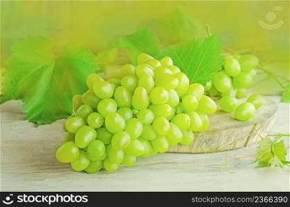Sweet green grape over the wooden background. Fresh green grapes. Bunch of grapes and vine leaf. White wine grapes. Grapes on a wooden table.