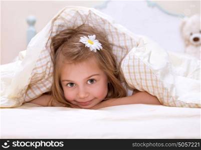 Sweet little girl lying down in the bed covered with blanket, cute flower in hair, sleeping in child bedroom, happy childhood concept