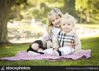 Sweet Little Girl Sitting with Her Baby Brother on a Picnic Blanket Outdoors at the Park.