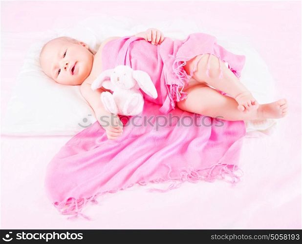 Sweet newborn baby lying down with rabbit soft toy, covered with pink scarf, happy childhood, innocence and tenderness concept
