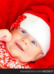 Sweet newborn baby wearing red Santa hat on Christmastime holidays, Christmas hat, New Year fun, funny facial expression, happy childhood concept