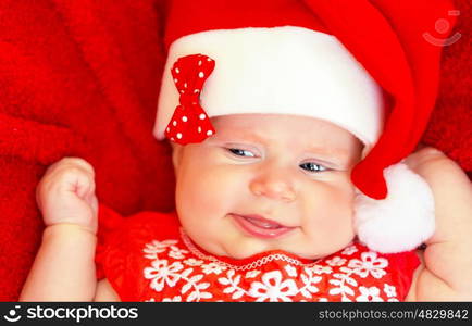 Sweet newborn baby wearing red Santa hat on Christmastime holidays, Christmas hat, New Year fun, funny facial expression, happy childhood concept