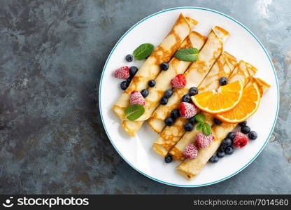 Sweet pancakes wrapped with fresh berries, crepes with blueberry and raspberry on breakfast, top view