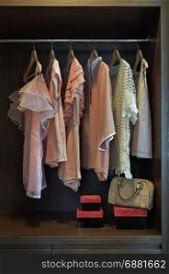 Sweet pastel blouses are hanging in open wooden wardrobe