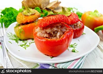 Sweet pepper stuffed with meat and rice in a plate on a napkin, fork, dill and parsley on a wooden boards background