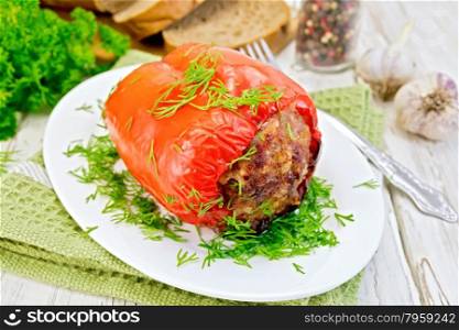 Sweet pepper stuffed with meat and rice with dill in a bowl on a napkin, fork, parsley and bread on the background light wooden boards