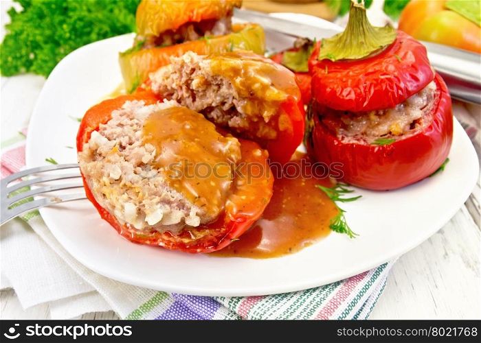 Sweet pepper stuffed with meat and rice with tomato sauce on a plate on a napkin, fork, dill, parsley on a wooden boards background