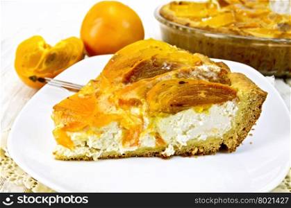 Sweet pie with curd and persimmons, a fork in the white plate on a napkin openwork silicon, glass pan with pie on the background light wooden boards