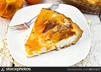 Sweet pie with curd and persimmons in a white plate, a fork in the white plate on a napkin openwork silicon, glass pan with pie on a wooden boards background