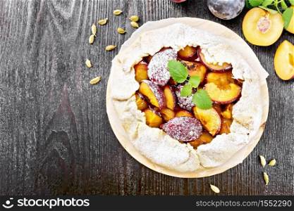 Sweet pie with plum, sugar and cardamom on parchment, sprigs of green mint on a wooden board background from above