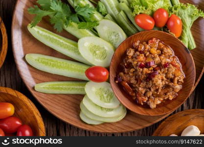 Sweet pork in a wooden bowl, put cucumber, long beans, tomatoes, and side dishes on a wooden table.