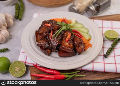 Sweet pork on a white plate with chopped scallions, chili, lime, cucumber, tomato, and garlic.