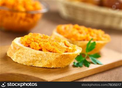 Sweet potato spread on baguette slice on wooden board with bread basket and bowl of sweet potato spread in the back (Selective Focus, Focus on the front of the spread) . Sweet Potato Spread on Baguette