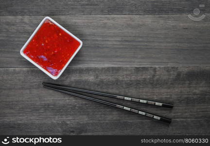 Sweet red sauce and chopsticks on an old wooden background.Top view