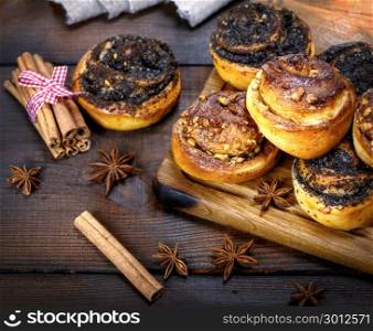 sweet round buns with cinnamon and poppy seeds on a brown wooden board,