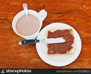 sweet sandwich from fresh toast with chocolate spread, table knife and cup of hot chocolate on wooden table