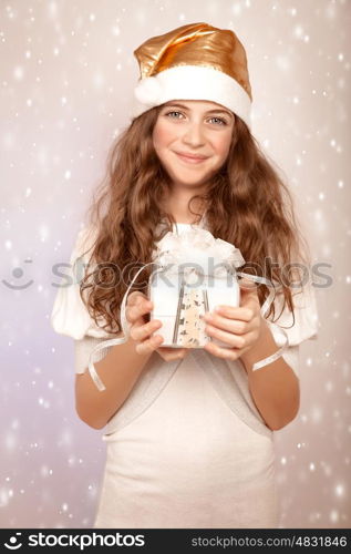 Sweet Santa helper, pretty teen girl wearing festive hat and holding in hands gift box, snow fall, Christmas party concept