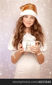 Sweet Santa helper, pretty teen girl wearing festive hat and holding in hands gift box, snow fall, Christmas party concept