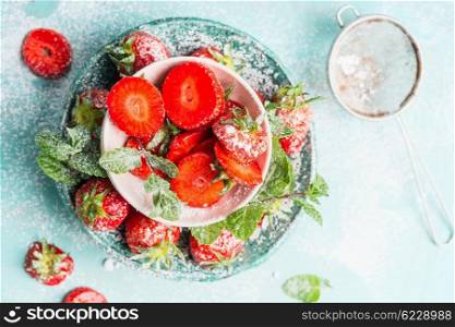 Sweet sliced Strawberries in bowls with icing sugar on light blue background, top view