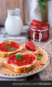 Sweet strawberry jam on toast close-up. Selective focus. The snack is decorated with mint leaves, vertical frame, close-up. Breakfast or lunch idea