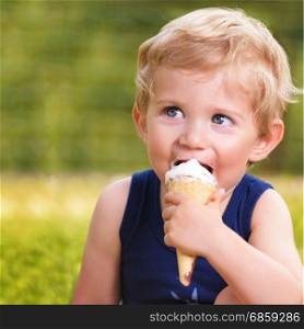 Sweet toddler baby boy eighteen months old, eating tasty ice cream over background with green bokeh outdoor.