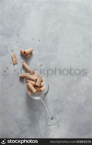 Sweet waffle crunchies in a glass spilled on a gray marble background with place under text.. A glass beaker with wafer tubules lies on a gray marble table.