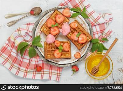 Sweet waffles with fresh strawberries, honey and ice cream on a beautiful plate, standing on a crumpled checkered napkin