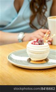 Sweet white cupcake with berries on the plate at the table on a woman’s background with a cup of coffee in a cafe. Sweet white cupcake with berries
