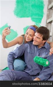 Sweet young couple taking self portraits while holding color roller at home