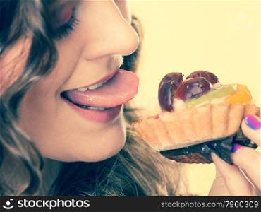 Sweetness and happiness concept. Closeup cute funny woman eating fruit cake cupcake having fun sticking tongue face profile yellow background