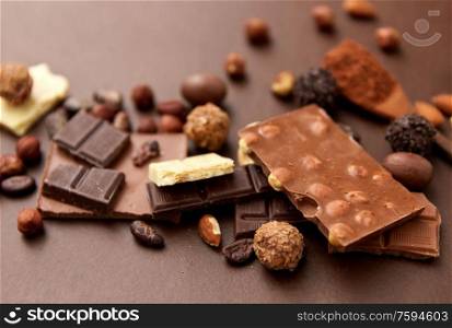 sweets and food concept - milk, dark and white chocolate bars with nuts, candies, cocoa beans and powder on brown background. chocolate with nuts, cocoa beans and powder